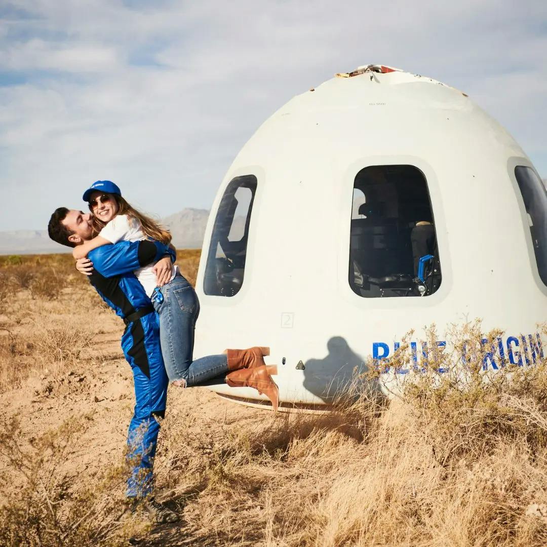 Victor Hespanha embracing his wife in front of a Blue Origin space capsule in a desert landscape.